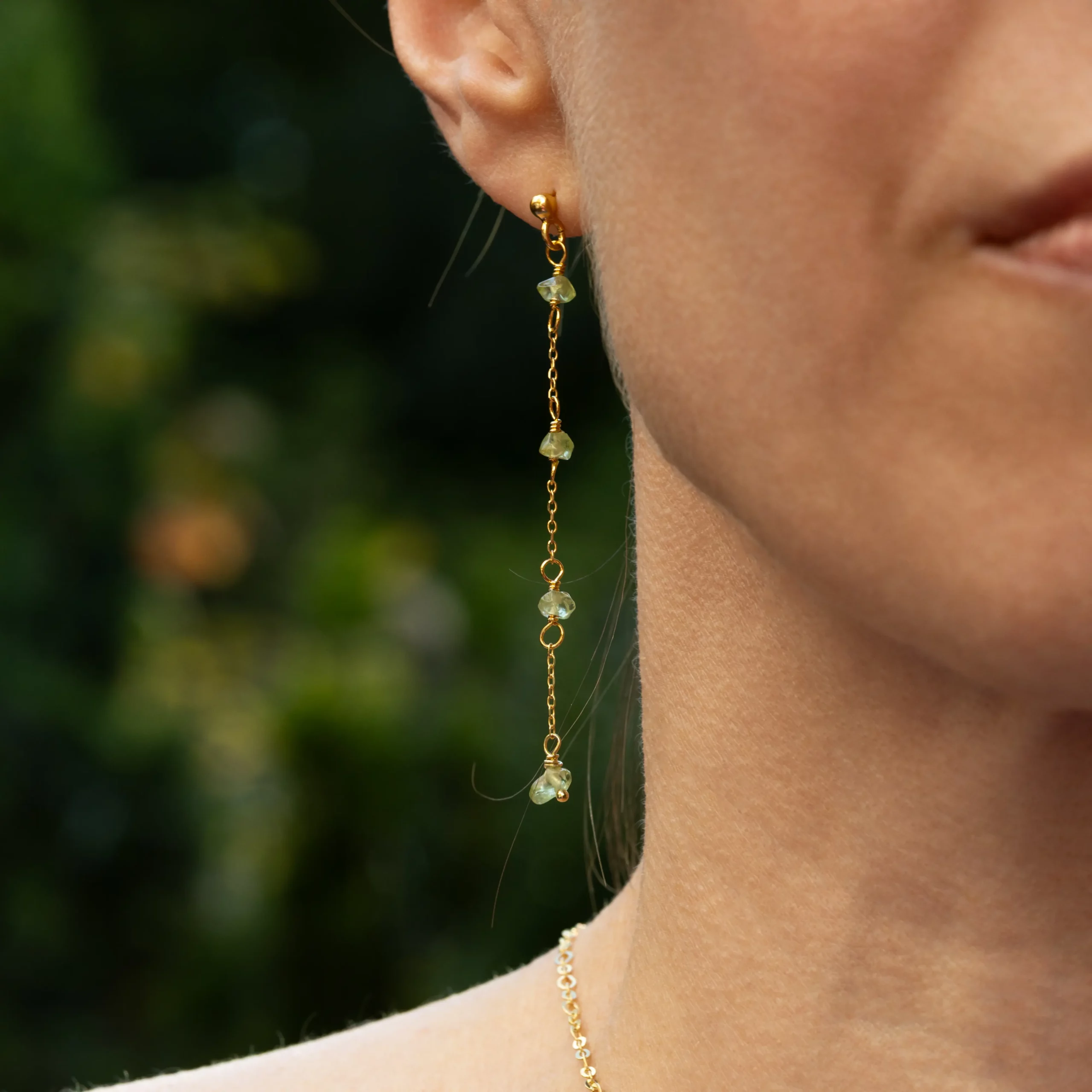 Pozłacane, srebrne, wiszące kolczyki z kolekcji Cuatro z zielonymi oliwinami na modelce.