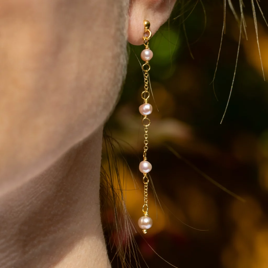 Kolczyki Cuatro pozłacane, srebrne, długie z perełkami słodkowodnymi na modelce.