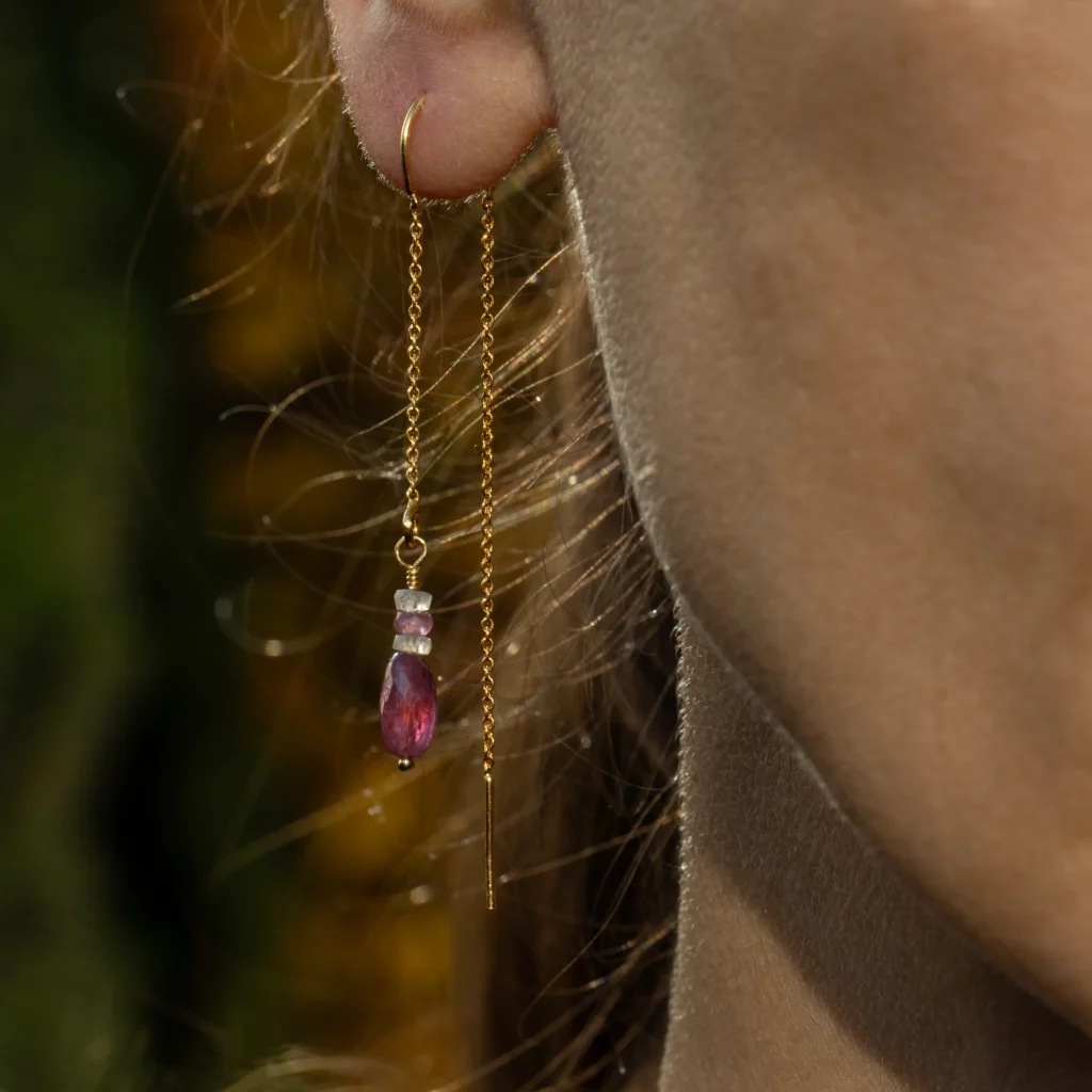 Przewlekane pozłacane srebrne kolczyki z kolekcji Continuo z dużym owalnym rubinem na łańcuszku, na modelce.