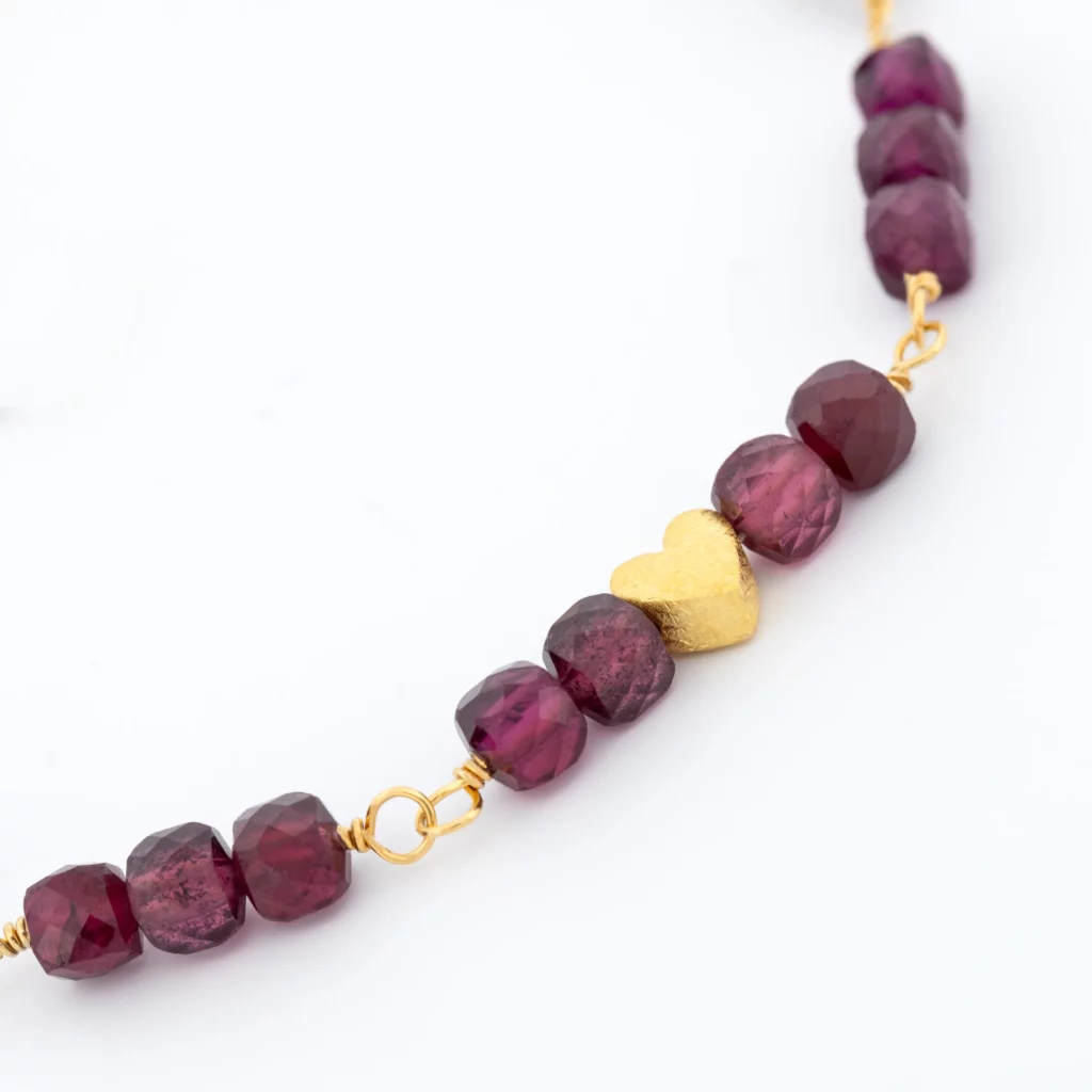 Detal bransoletki srebrenej, pozłacanej z naturalnym granatem i motywem serca.