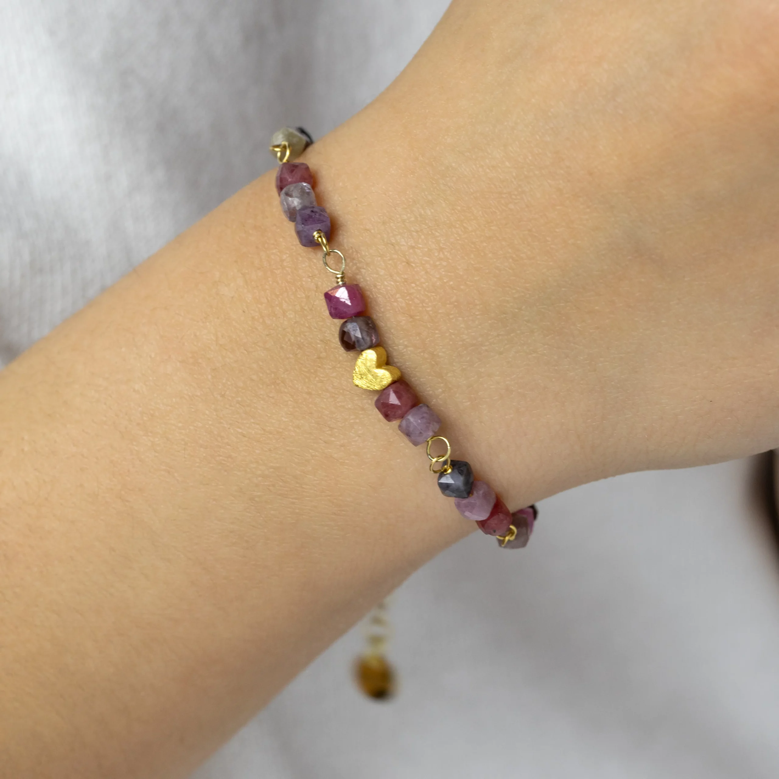 Bransoletka Serce z kolorowymi naturalnymi spinelami, wykonana z pozłacanego srebra na nadgarstku.